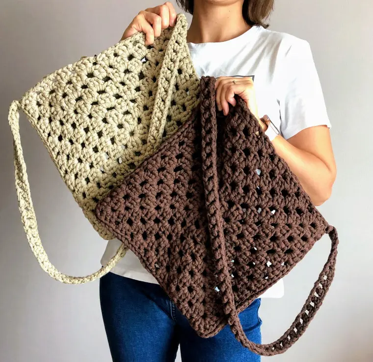 Woman holding two crochet granny stitch bags, one off white, one chocolate brown.