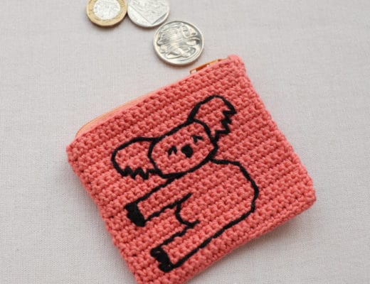 The Crochet Koala Coin Purse laid on a white surface with coin coming out